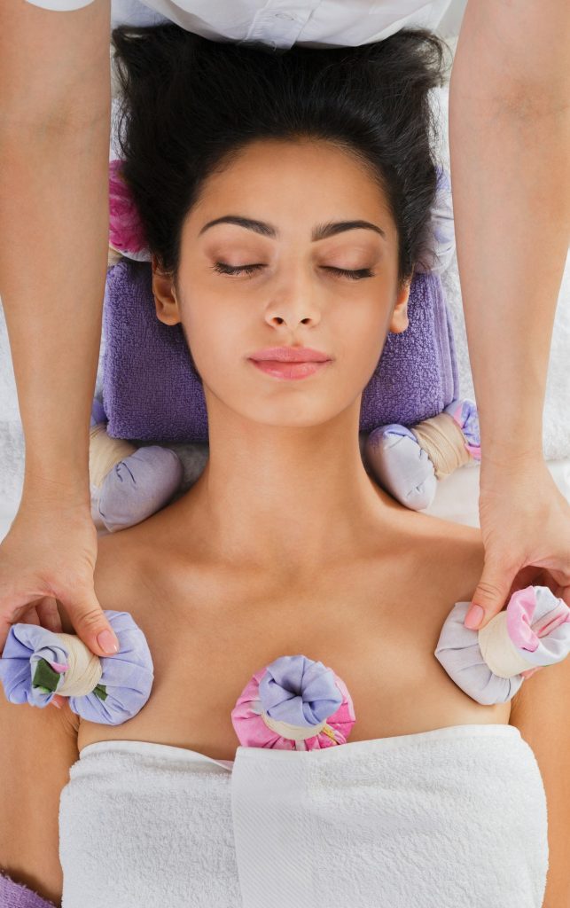 Woman has herbal ball massage in ayurveda spa wellness center