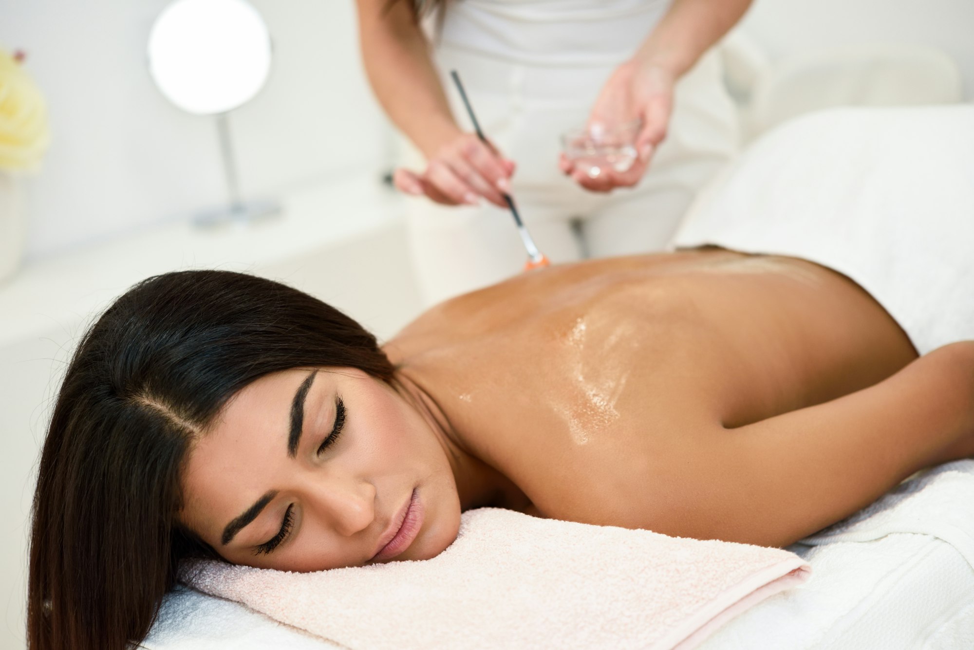 Woman receiving back massage treatment with oil brush in spa wel